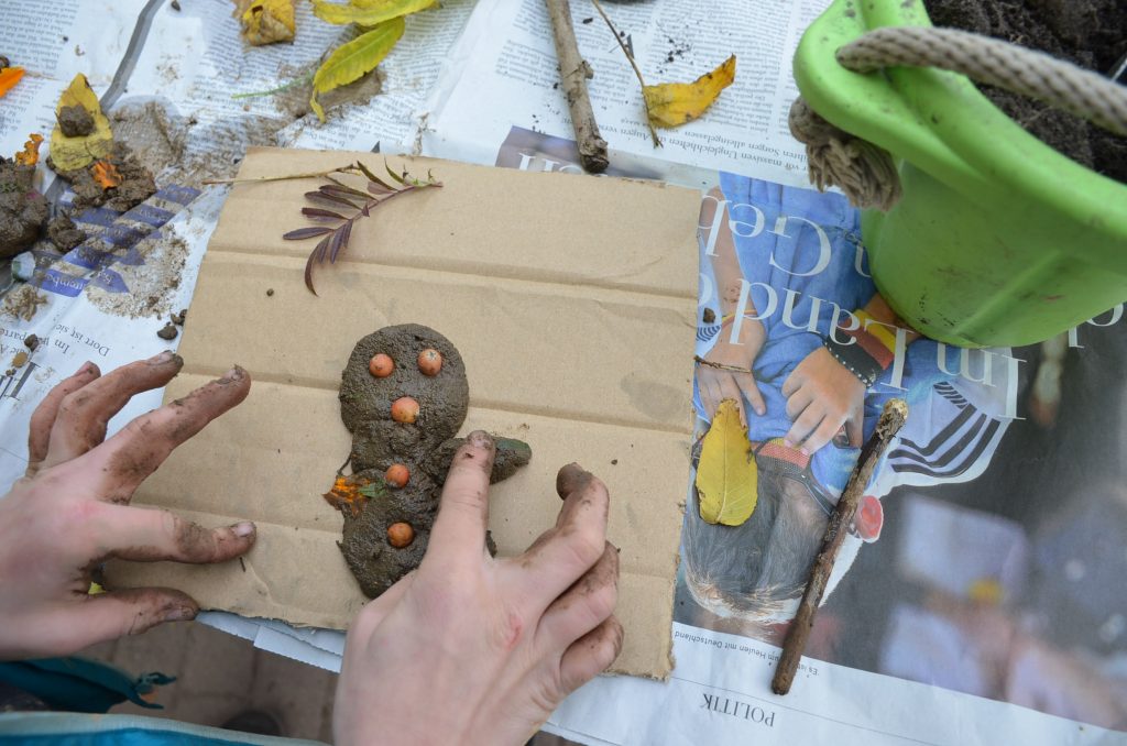 Pappe mit Figur aus Matsch und Kinderhände